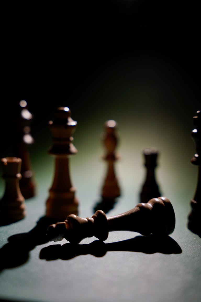 Dramatic chess scene highlighting a fallen king piece amidst shadows.