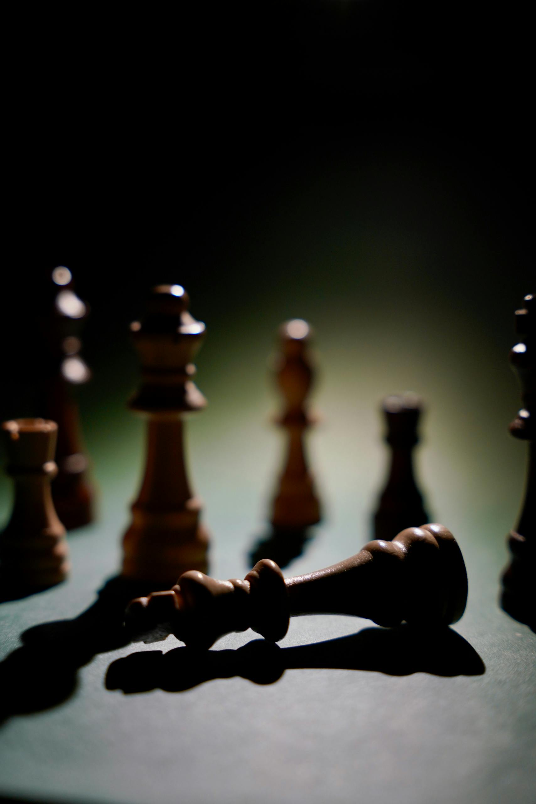 Dramatic chess scene highlighting a fallen king piece amidst shadows.